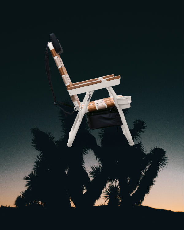 Side view of PARKIT Eclipse Recliner outdoor chair with cooler storage and cupholder, displayed against desert palm silhouette at sunset.