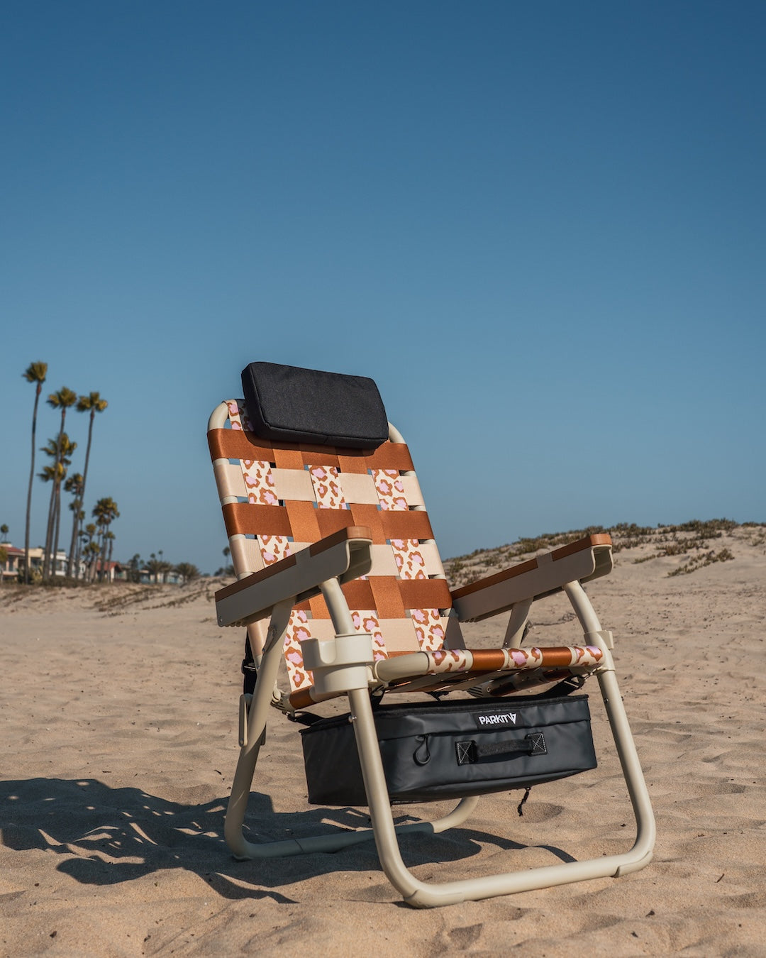 PARKIT Eclipse Recliner outdoor beach chair in leopard print Wild 4 Boobies design, shown on desert sand with palm trees in background.