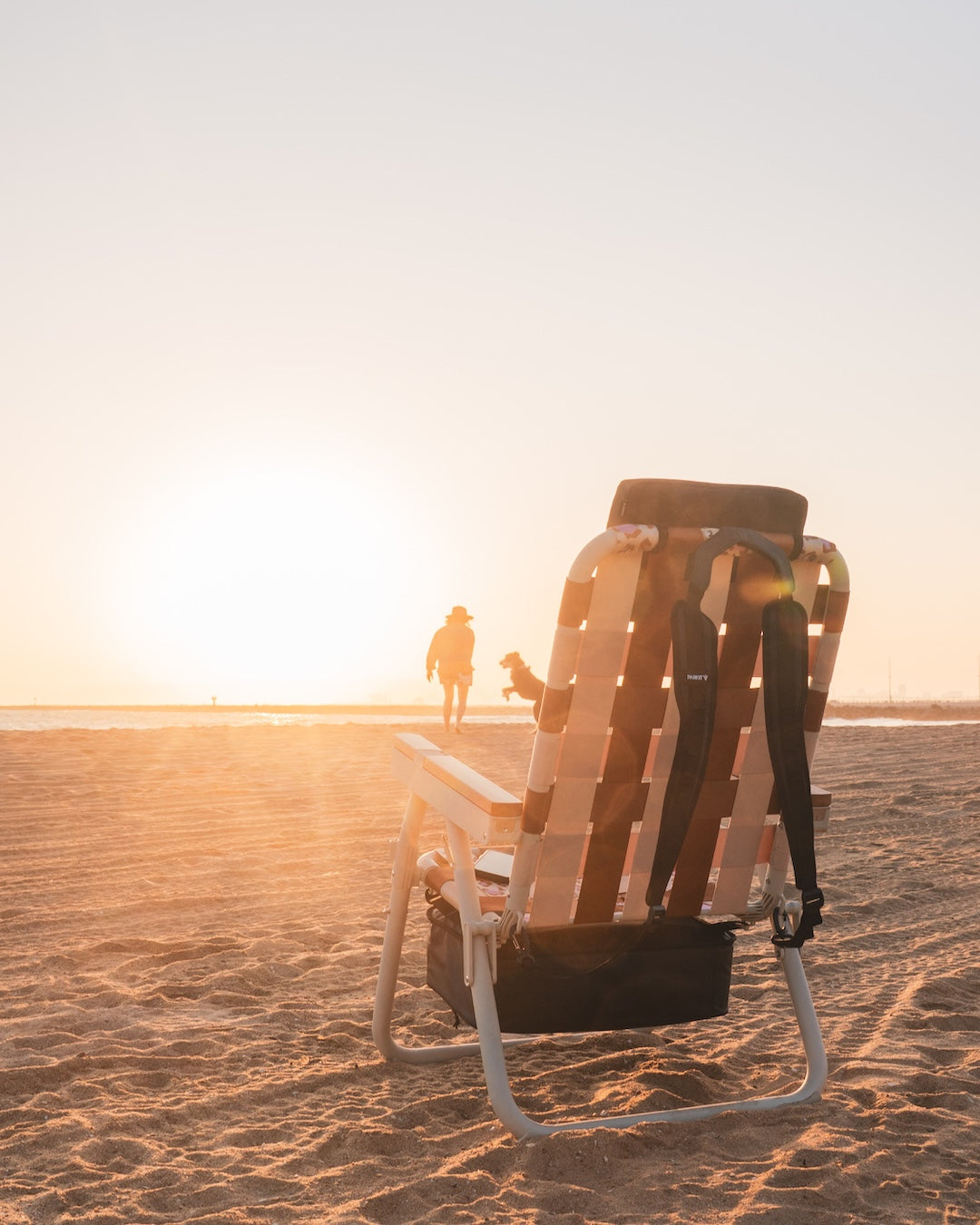 PARKIT Eclipse Recliner beach chair in Wild 4 Boobies pink at sunset, with surfer Jodie Nelson playing with her dog near the shoreline