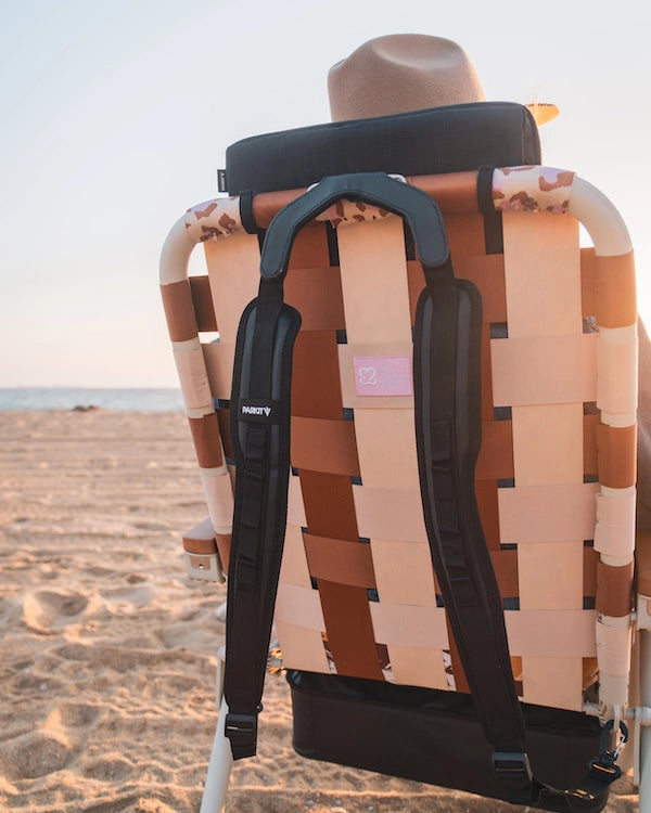 Back view of PARKIT Eclipse Recliner Wild 4 Boobies edition with padded backpack straps and Keep A Breast logo patch, set on sandy beach at sunset.