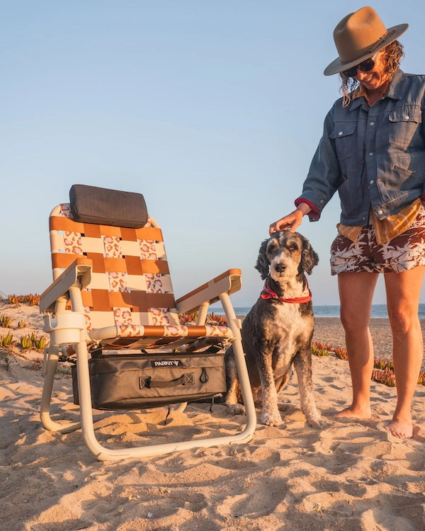 PARKIT Eclipse Recliner Wild 4 Boobies leopard print beach chair with cooler storage, photographed at sunset with Jodie Nelson petting her dog on the sand.