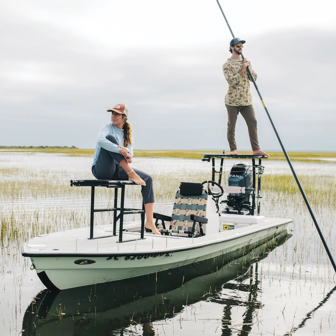 Two people on a boat in a marshy area with grass and water with a PARKIT Eclipse chair in the middle of their boat