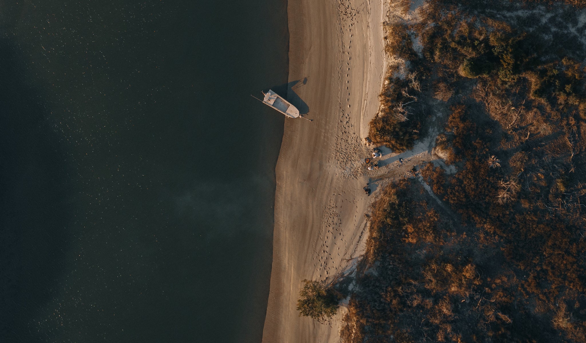 A drone shot of a skiff style boat parked on the sandbar as friends enjoy a campfire with their Voyager outdoor chairs.