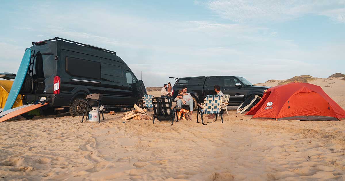 PARKIT chair unfolded next to a campervan in the dunes, with beer in the chair's cup holder, showcasing campervan accessories for van life.