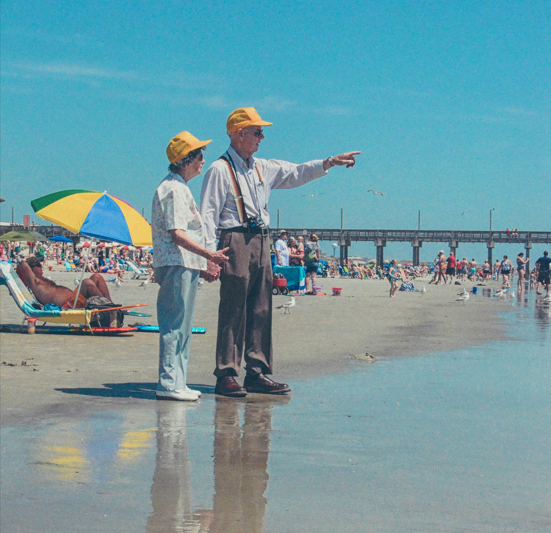 two older people at the beach pointing at the water