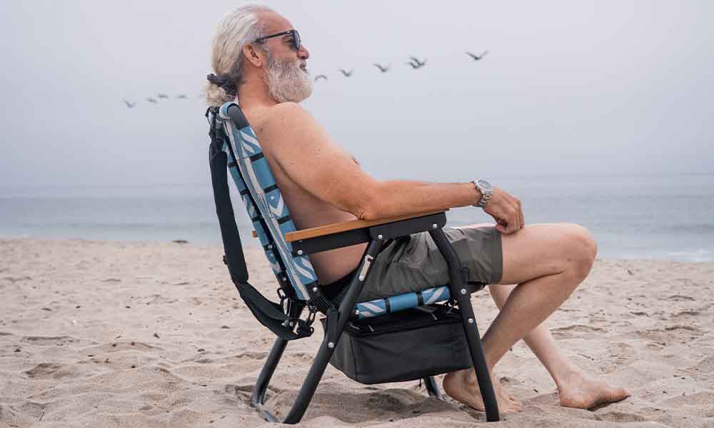 Senior enjoying the beach in a PARKIT Voyager chair with a cold drink and relaxed posture