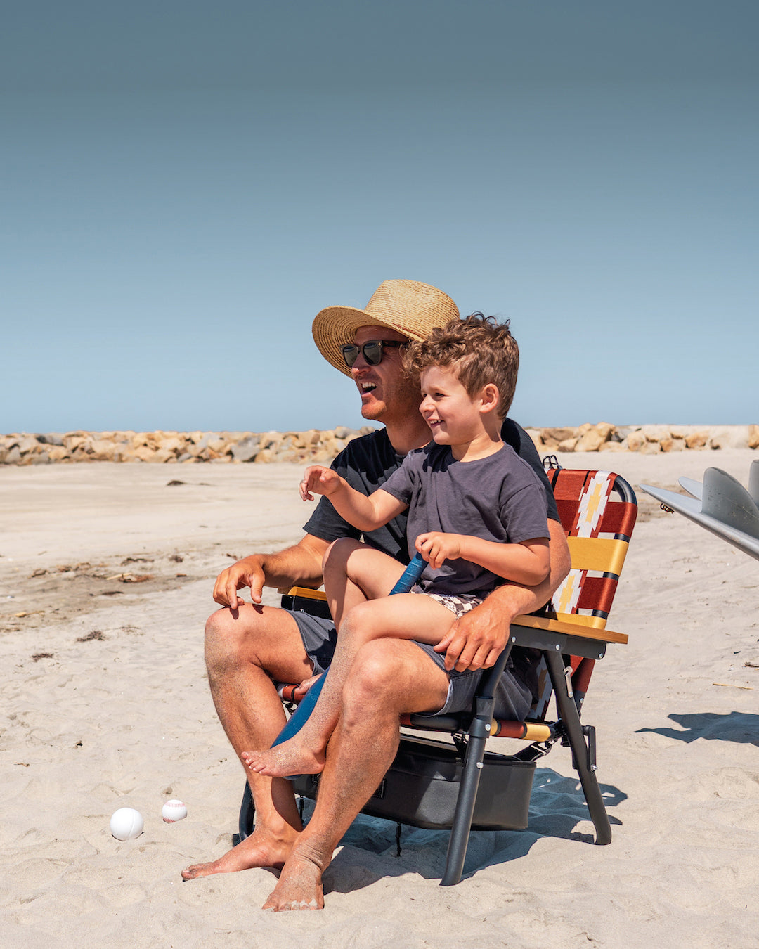 a father and son sitting on a beach chair at the beach 