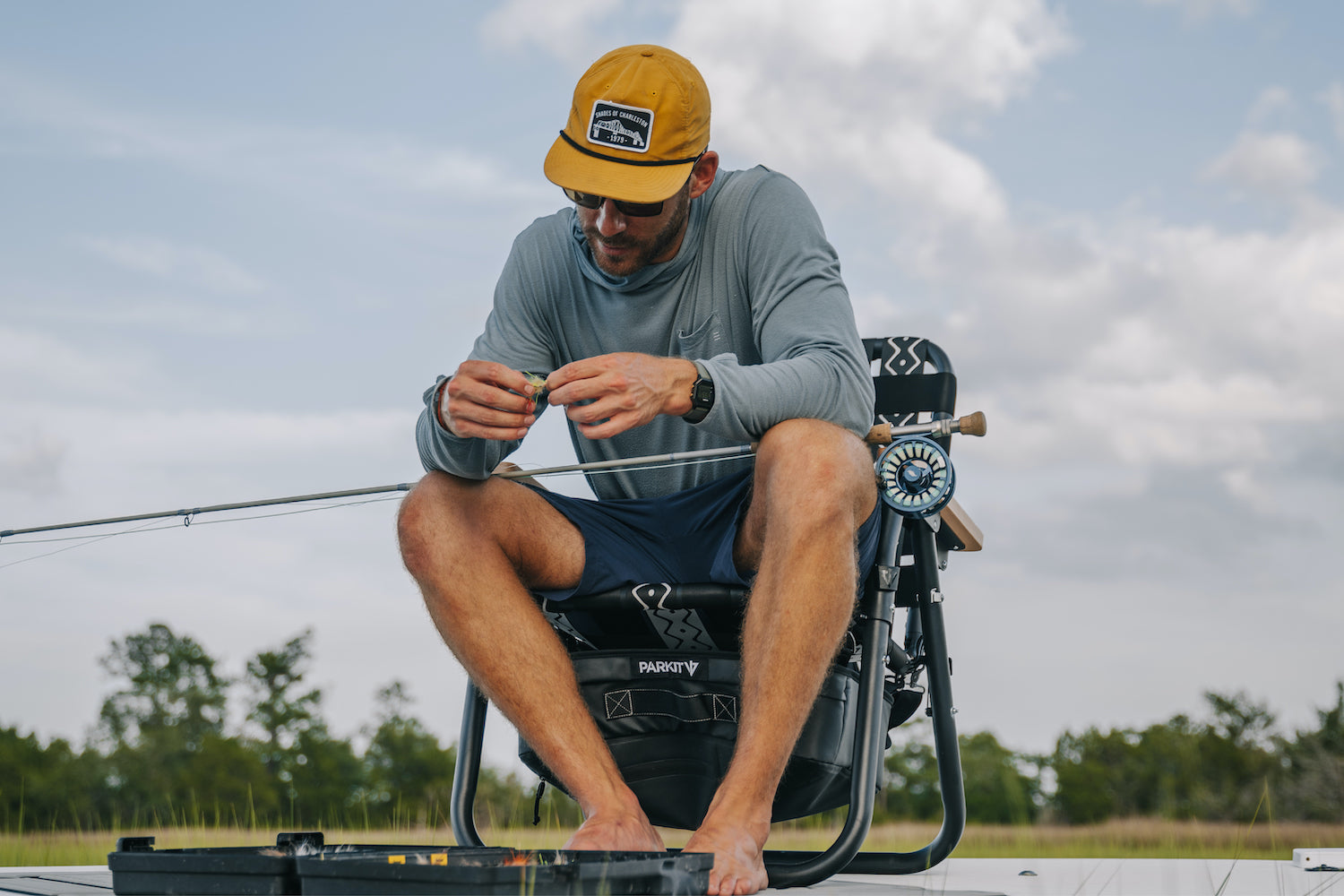 A Man setting up his fly fishing pole while sitting on his skiff in a Voyager outdoor chair.