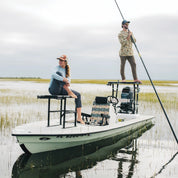 Two people on a boat in a marshy area with grass and water with a PARKIT Eclipse chair in the middle of their boat