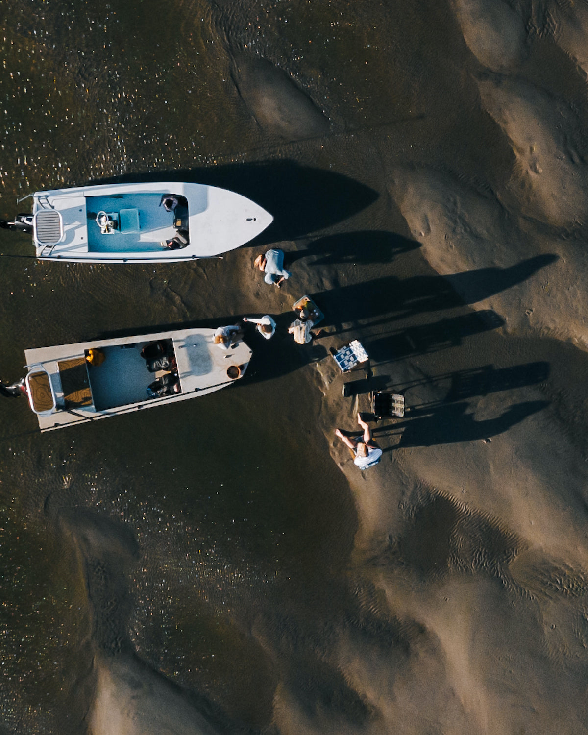 2 Skiff Boats on shore with friends playing on the sand as Voyager outdoor chair sit in the forground