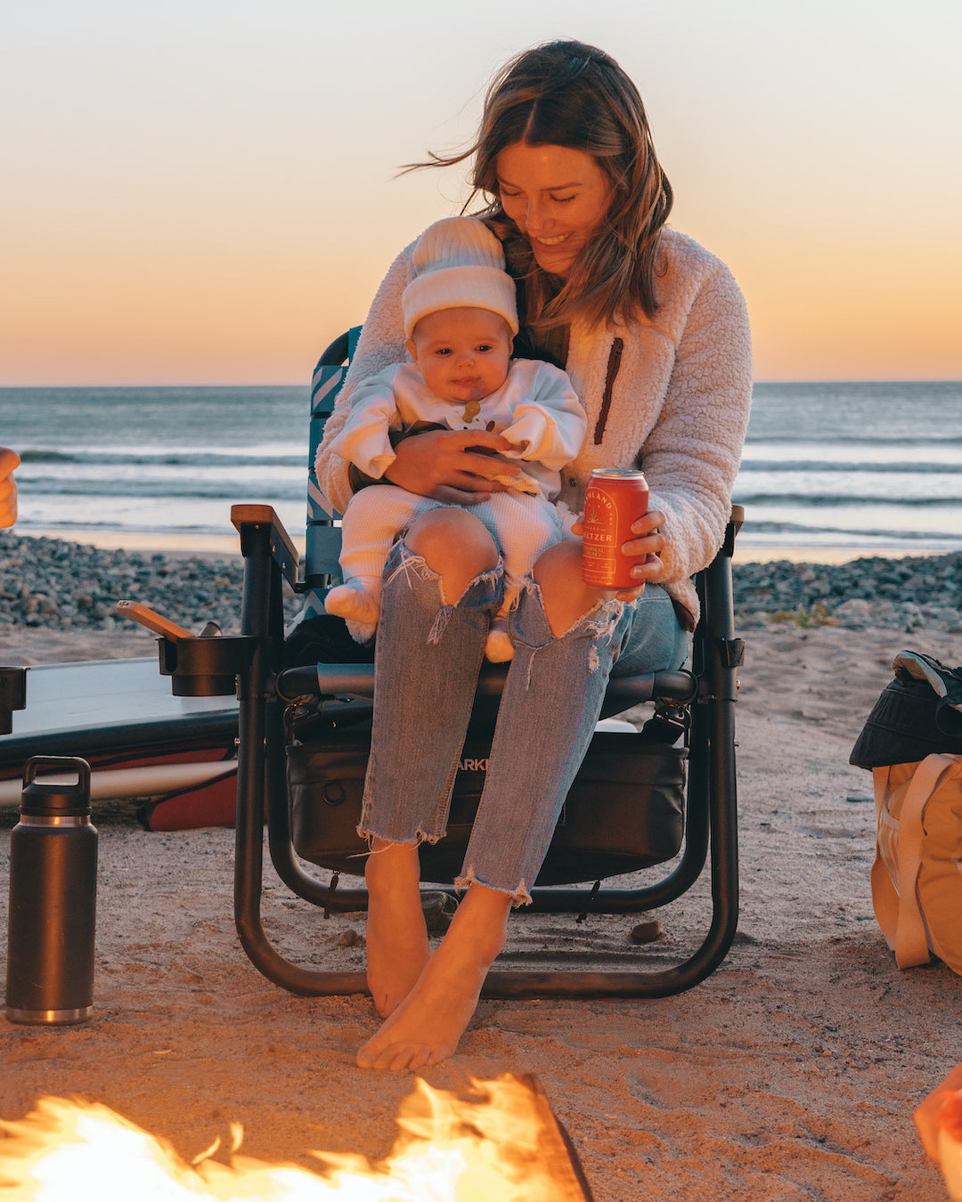 A mom with her baby sitting in her lap as she watches her baby girl experience here first campfire while sitting in a Voyager Outdoor chair.
