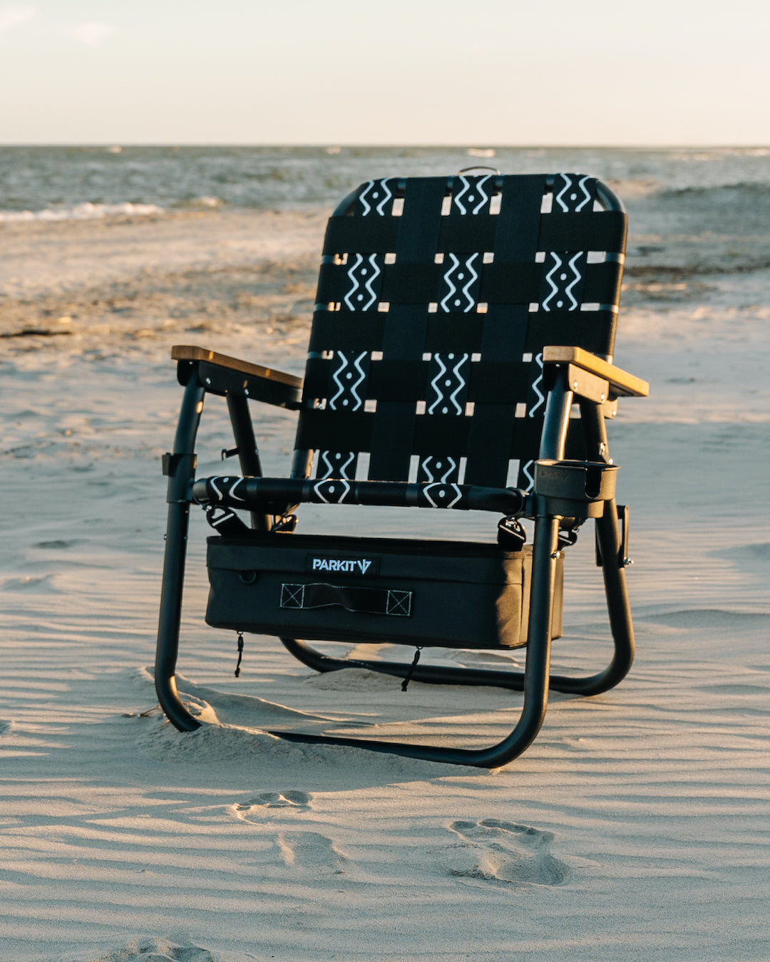 A single beach chair sitting in the sand with the ocean in the back 