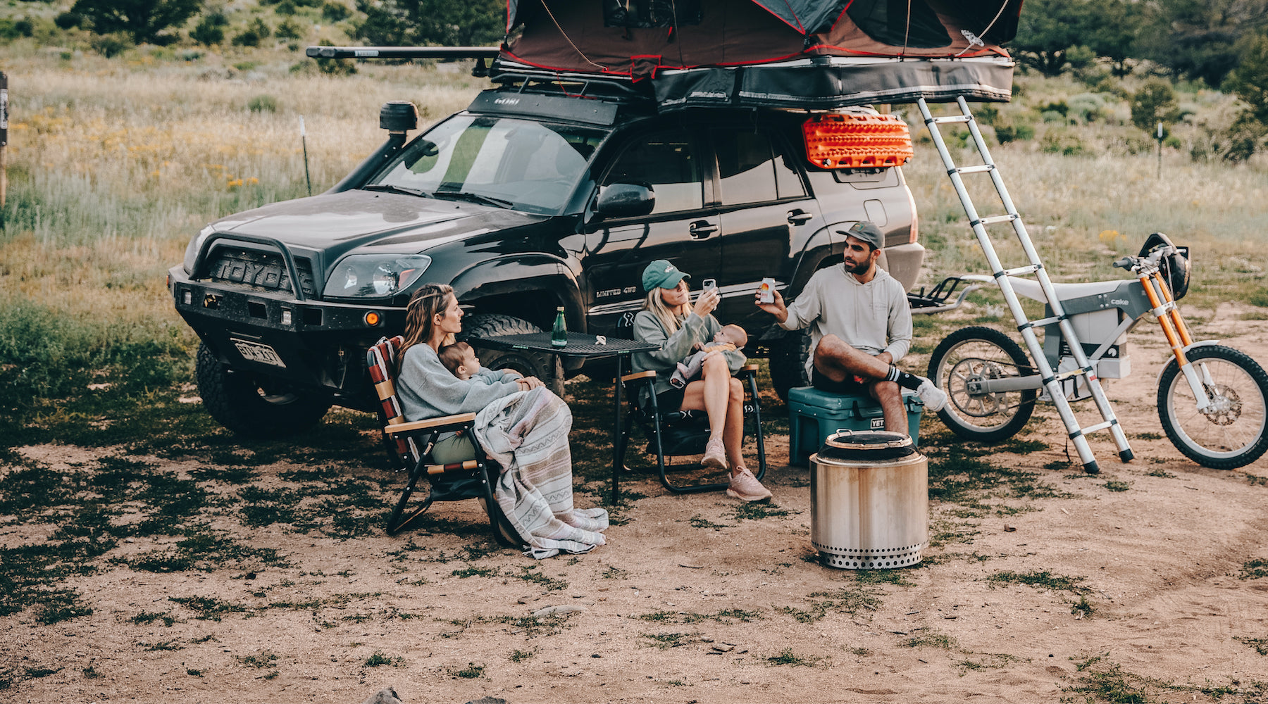 A family sitting in their voyager outdoor chairs with their full camping set up which includes a converted toyota 4runner and solo stove with pop-top tent on the roof.