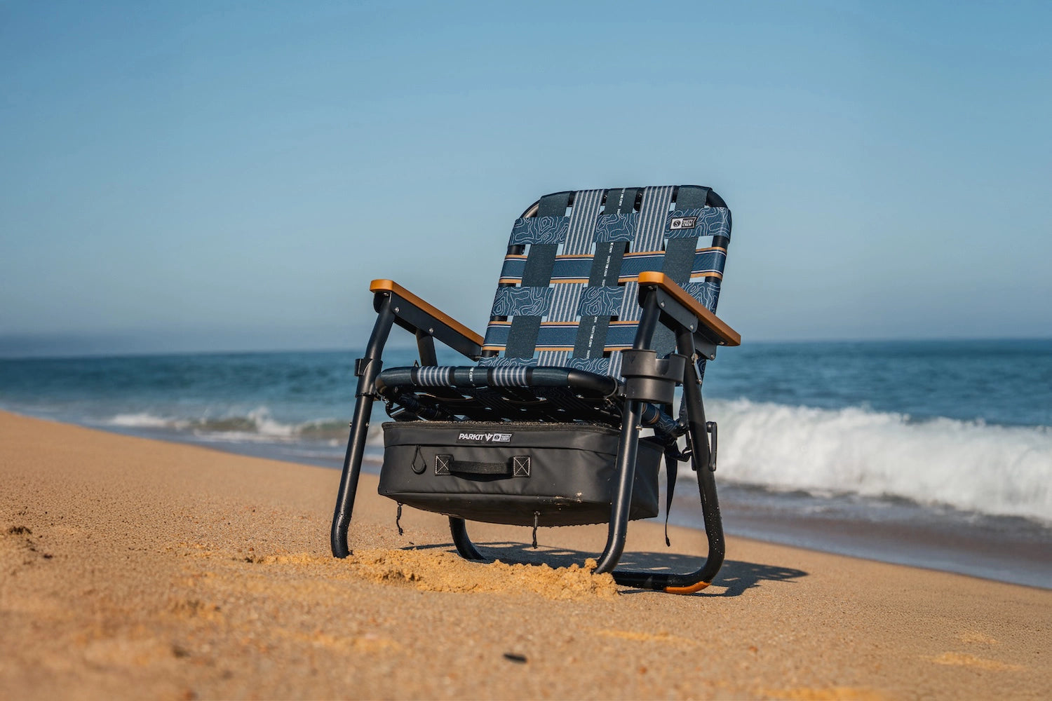 rust proof and salt proof and beach proof voyager becah chair from PARKIT and Salty crew sitting on a white sandy beach with waves crashing in the background. 