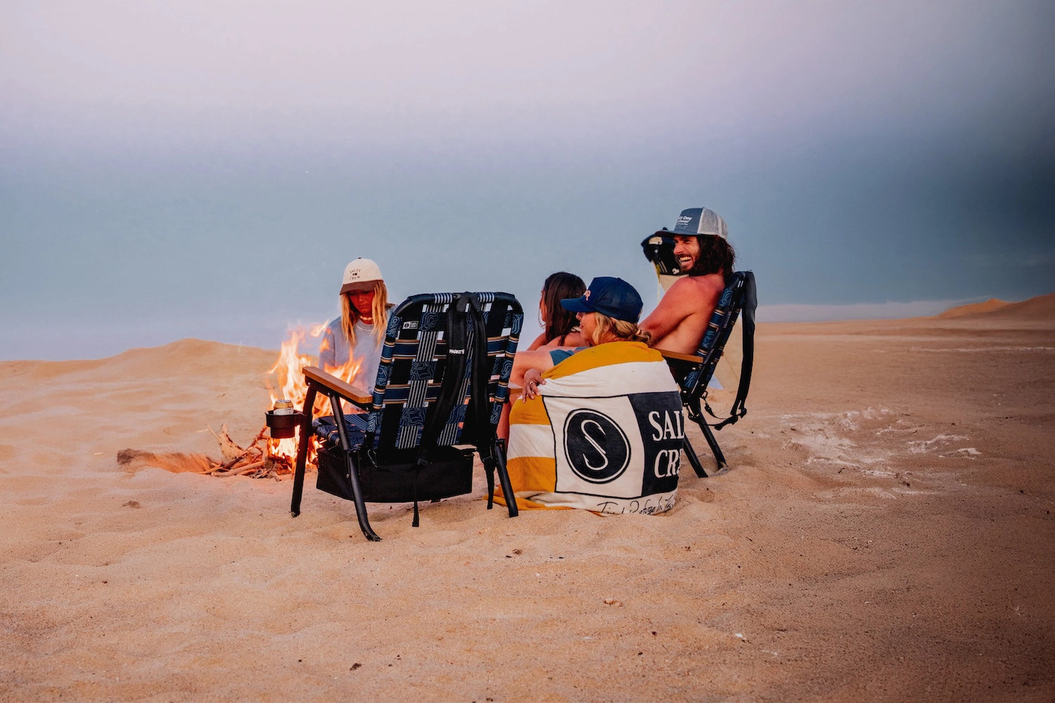 friends sitting around a fire at the end of the day enjoying their voyager beach and boat chair built by a collaboration between Salty Crew and PARKIT. 