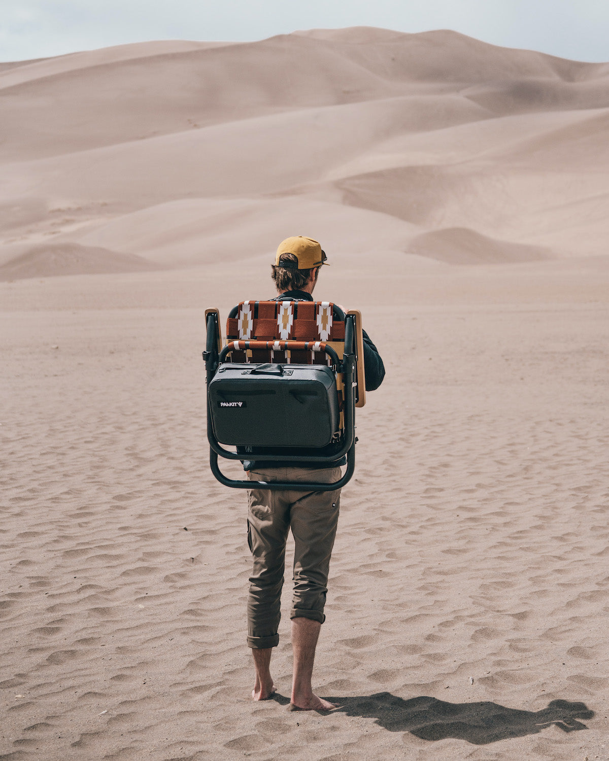 A man standing while wearing the Voyager outdoor chair as a backpack with the great sandune national park in the background