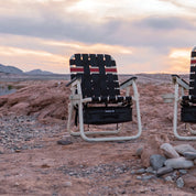 Foldable chair with a striped pattern in a desert landscape during sunset.