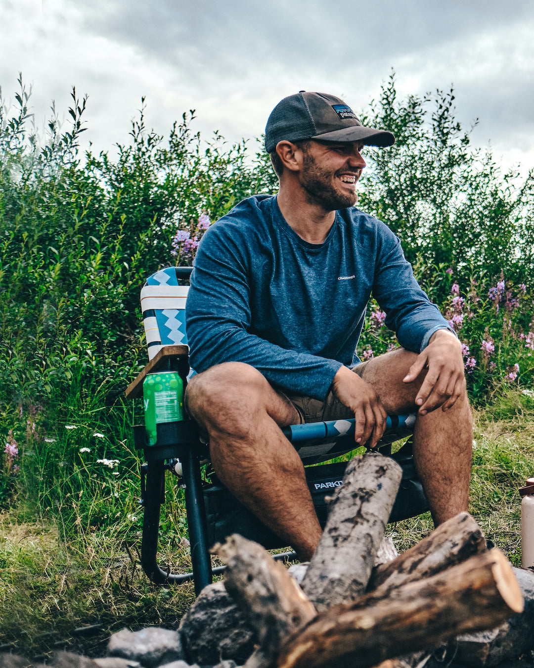 A man and his dog sit around a campfire in their Classic Blue Voyager outdoor chairs from PARKIT.